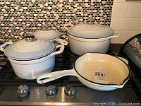 White enamel pots and frying pan set displayed on stove, showing condition and minor enamel loss