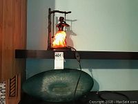 Figural lamp lit depicting a woman on a swing with glowing skirt on upper shelf, green art glass lamp below