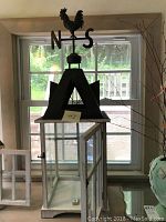 Full view of the large candle house with glass panels and metal A-frame roof with rooster weathervane on top