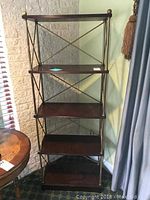 Full view of the five tier shelving unit with wood shelves and brass-finish metal frame with cross braces.