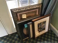 Four framed pieces stacked leaning against a window, showing vibrant different frame styles and sizes, including a shadow box frame.