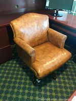 Front view of brown leather swivel office chair showing cushioned seat, back, and armrests, on caster wheels beneath a desk.