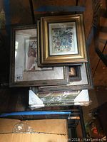 Stack of seven framed prints laid on a floor, showing edge of frames and glass reflecting light