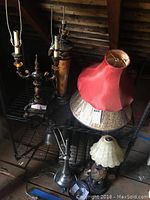 Four lamps and two lampshades together on shelving in dimly lit attic/storage area.