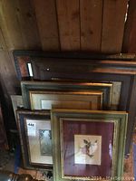 Stack of six picture frames leaning against a wooden wall, showing a variety of sizes and frame styles.