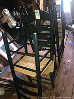 Photo showing four black ladder back chairs stacked together, displaying their woven rush seats and turned finials.