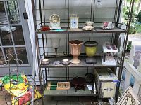 Front view of five shelf metal unit with various decorative items including clocks, planters, candle holders, and boxes