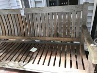 Front and angled views showing weathered teak bench with slatted design, wooden armrests, and visible natural wear due to exposure.