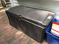 Wide view of Suncast outdoor storage bin showing rectangular shape and woven resin design with closed lid.