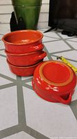 Four red ceramic ramekin bowls stacked with one bowl flipped to show bottom, displaying their size and glossy finish.