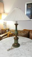 Full view of the metal base table lamp showing its green and bronze cylindrical base with pleated white silk shade on a marble table.