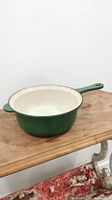 Side angle view of vintage green Le Creuset cast iron pan resting on wooden surface.