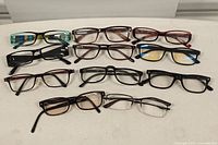A top view of 11 assorted eyeglasses frames arranged on a white surface, showing various colors and styles.