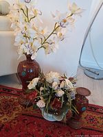 Photo showing all three items displayed together: tall brown vase with artificial white orchids, medium vase, and small flower arrangement in scalloped bowl.
