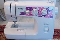 Full front view of the Brother LS-2000 sewing machine showing floral decal, control dials, needle plate, and storage compartment.