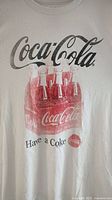 Front view of white Coca Cola t-shirt with six-pack bottle graphic and text 'Have a Coke'.