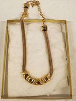 Front view of gold-tone ladies necklace on white cushion with gold-trimmed box