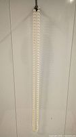 Full length view of 27 inch faux pearl necklace hanging vertically against white background.