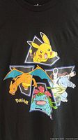 Front view of black Pokemon T-shirt showing colorful Pikachu, Charizard, Venusaur, and Blastoise print.