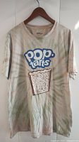 Full view of Pop Tarts graphic t-shirt hanging on wooden hanger, showing faded and stained beige fabric with logo and pastry print.