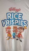 Front of white T-shirt showing Kellogg's Rice Krispies logo and cartoon characters Snap, Crackle, and Pop in color.