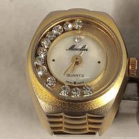 Close-up front photo of gold-tone ring watch with rhinestones around the dial, showing the Moulin branding and Quartz movement indication.