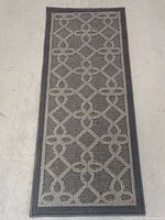 Top view of rectangular rug showing geometric diamond and floral pattern in beige on gray background with bordered edges.