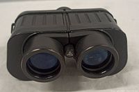Front view of black compact T7006 binoculars showing both large round objective lenses and central hinge with T7006 emblem.