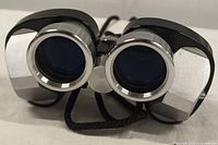 Front view of compact black and silver vintage binoculars showing front lenses and attached black strap.