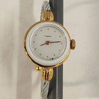 Close-up photo of Timex watch face showing white dial with gold dot markers and gold-tone bezel and crown.