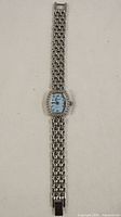 Full view of silver-tone linked bracelet watch with rectangular embellished face and blue dial.
