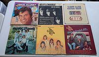 Top-view photo of six vinyl record covers showing classic rock and pop bands including Dick Clark compilation, The Beatles, James Gang, The Ventures, and The Grass Roots.