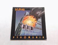 Front cover of Def Leppard Pyromania vinyl LP showing album artwork with shattered glass and fiery explosion building reflection.