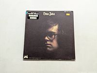 Front cover of Elton John LP, close-up portrait of artist with glasses, sticker indicating the original soundtrack for a Border Song.