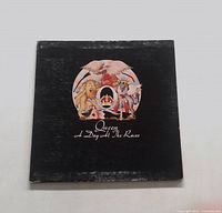 Front cover of Queen A Day at the Races album, showing the colorful Queen crest logo on a black background.