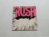 Front cover of Rush self-titled LP album with 'RUSH' in large pink letters on a black and white burst background.