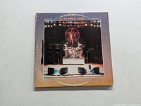 Front cover of Rush 'All The World's A Stage' vinyl album showing drum kit on stage and large band logo in red.