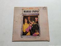 Front cover of The Mamas & The Papas self-titled LP showing band members through a window frame design, cover has visible wear and marks.