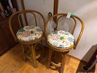 View of two wood frame bar stools with floral upholstered swivel seats side by side.