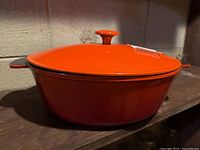 Orange cast iron Dutch oven with lid on shelf
