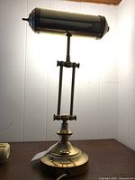 Articulated brass desk lamp showing front and side profiles, against a white paneled wall.