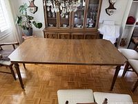 View of full dining table with two leaves attached, showing top surface and legs around it in a room with other furniture.