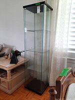 Full view of the tall glass display cabinet positioned next to a side table showing the overall structure and glass shelves inside.