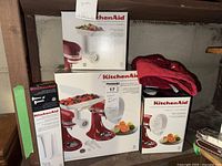 Photo of boxed KitchenAid food grinder, citrus juicer, and sausage stuffer attachments for stand mixers.