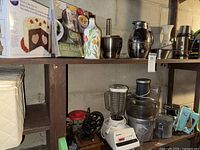Wide shot of two wooden shelves featuring kitchenware including a vintage Osterizer blender, hand mixer, juicers, pestle and mortar, Wilton heart-shaped cake pan, and other items.