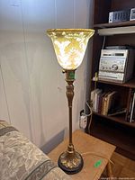 Photo of single table lamp showing metal base with leaf design and yellow floral patterned flared glass shade