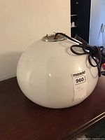 White globe light fixture showing front view with cord coiled on top, placed on wooden surface.