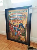 Framed comic poster of Captain America and The Falcon leaning against wall on parquet floor.