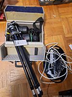Pentax camera, tripod, cords, and tool case in open view on floor
