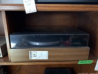 Turntable inside shelving unit with dust cover on, showing wood grain base and black dust cover.
